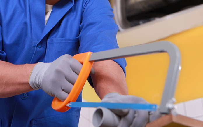 Hombre con manos enguantadas corta tubos de pvc con una sierra para metales naranja