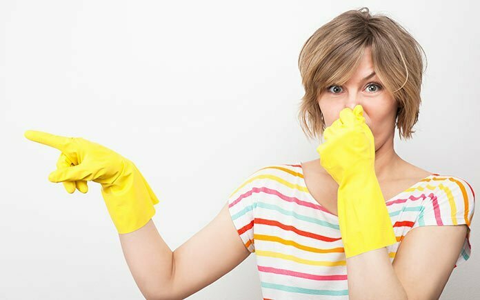 Mujer con guantes de goma, tapándose la nariz y apuntando a un lavavajillas maloliente